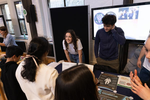 Two students stand behind the Space Lab stall the Insights Festival and speak to attendees