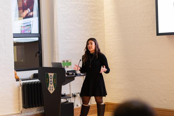 A student speaks at the lecture podium while gesticulating 