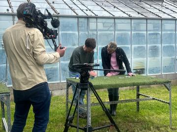 Dr Jonathan Pattrick provides a live demonstration with honeybees, standing next to a BBC presenter, in front of several filming cameras 