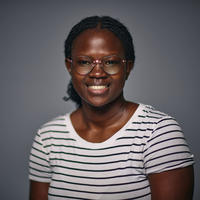 A woman with dark skin, black hair and eyes. She is wearing glasses and a striped shirt.