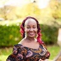 A woman with dark skin and red braids. She is wearing an African print summer dress.
